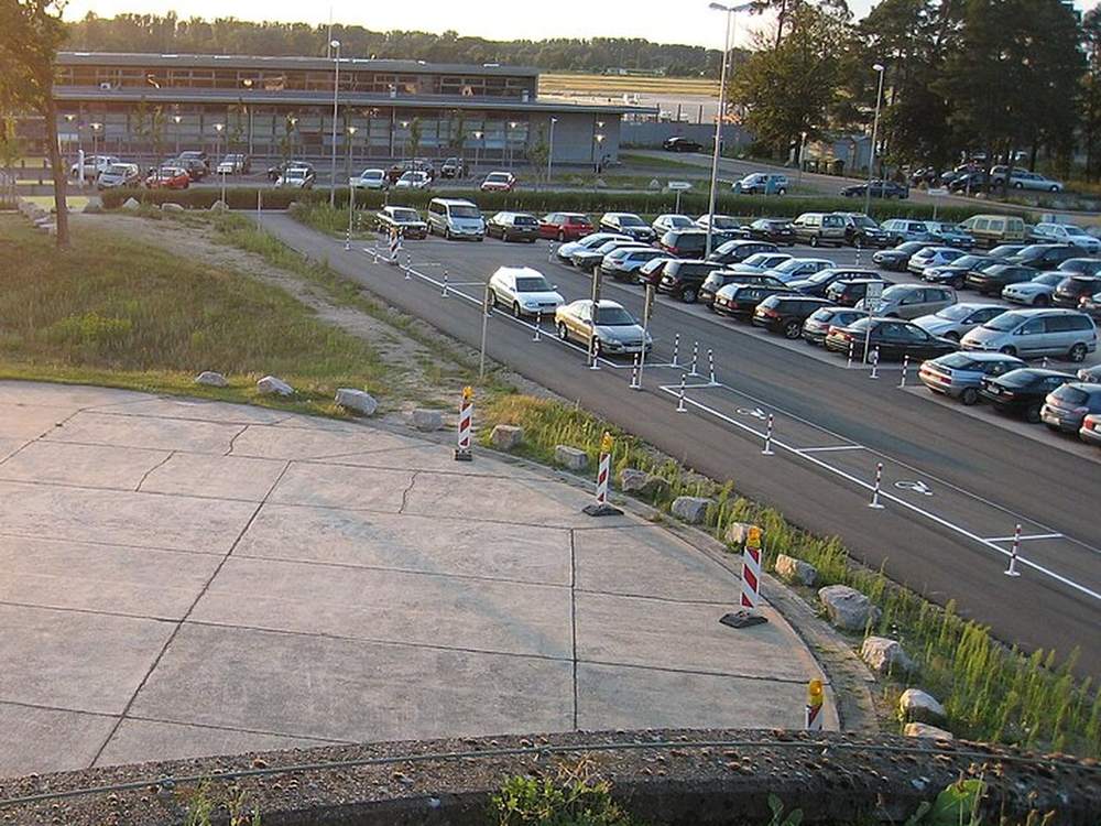 Parkfläche am Flughafen Karlsruhe/Baden-Baden mit abgestellten Fahrzeugen, im Hintergrund die Flughafengebäude